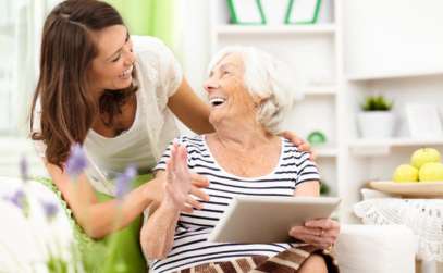 a caregiver laughing with a senior woman while she holds an ipad