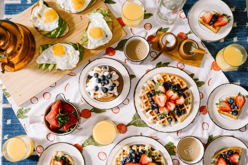 a table full of waffles, eggs, toast, fruit, and juice