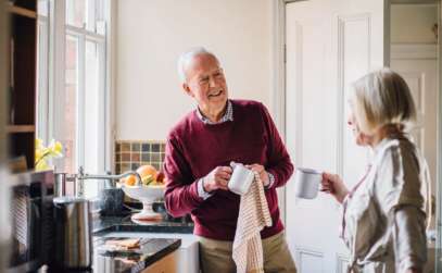 an elderly couple holding coffee mugs in a kitchen