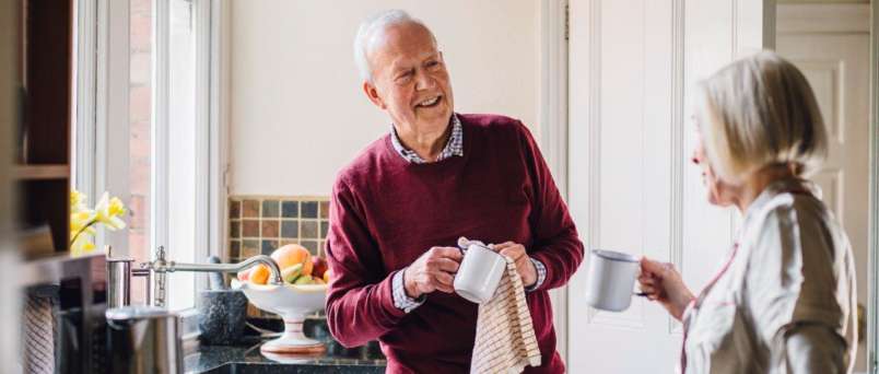 an elderly couple holding coffee mugs in a kitchen